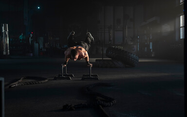 Strong muscular man working out in the gym doing a handstand exercise on stands, amazing fitness moments in the gym