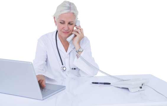 Doctor talking on landline phone while using laptop at desk