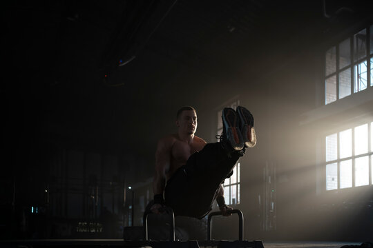 Young muscular sportsman doing straddle planche on parallel bars while training in the gym