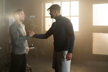Young male trainer handshaking with mid age client after training session in the gym