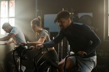 Intense bicycle workout at the gym of active athletic people in training. Young diverse group in fitness power cycling for muscle, weight loss and exercising strength