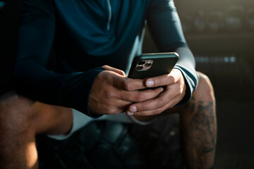 Lifestyle portrait of a handsome muscular man with phone sitting on the tyre in the gym