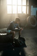 Young tired fitness man using smartphone in gym. Looking at screen of smartphone, chat with someone