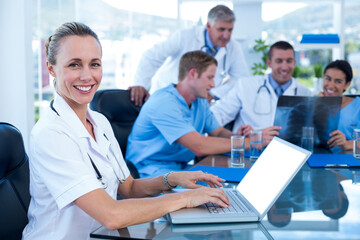 Beautiful smiling doctor typing on keyboard with her team behind