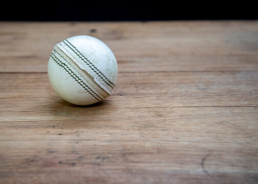 Old white leather cricket ball isolated against a wooden background.