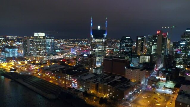 Aerial Shot Of Illuminated Skyscraper In Residential City, Drone Flying Backwards Over Cumberland River At Night - Nashville, Tennessee