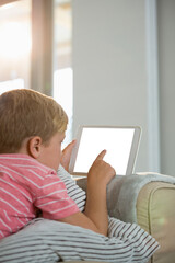 Boy using digital tablet while sitting on sofa in living room