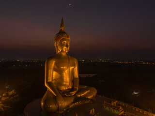 aerial view The moon was above the head of the biggest golden Buddha in the world..scenery red sky in twilight background. .golden big buddha is a popular landmark at wat Muang Ang Thong Thailand.