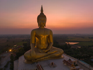 Obraz premium aerial view The moon was above the head of the biggest golden Buddha in the world..scenery red sky in twilight background. .golden big buddha is a popular landmark at wat Muang Ang Thong Thailand.