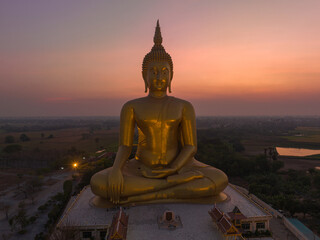Obraz premium aerial view The moon was above the head of the biggest golden Buddha in the world..scenery red sky in twilight background. .golden big buddha is a popular landmark at wat Muang Ang Thong Thailand.