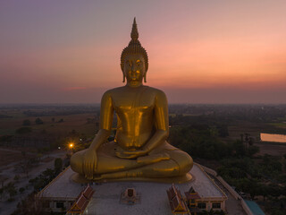 aerial view The moon was above the head of the biggest golden Buddha in the world..scenery red sky in twilight background. .golden big buddha is a popular landmark at wat Muang Ang Thong Thailand.