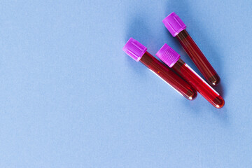 Three blood sample tubes with purple lids, on blue background with copy space