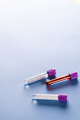 Three sample tubes with purple lids, one containing blood, on blue background with copy space