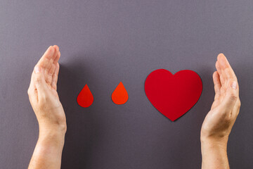 Hands of caucasian woman protecting blood drops and heart, on grey background