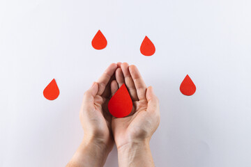 Hands of caucasian woman cupping blood drop, with blood drops on white background