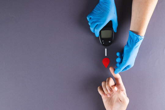 Hands of gloved doctor with glucometer taking blood sugar reading from caucasian woman, copy space