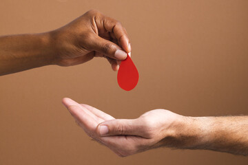 Hands of biracial man giving blood drop to caucasian man, on brown background - Powered by Adobe