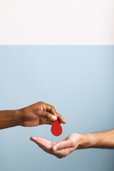 Hands of biracial man giving blood drop to caucasian man, on blue and white background, copy space
