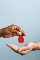 Hands of biracial man giving blood drop to caucasian man, on blue background with copy space - obrazy, fototapety, plakaty