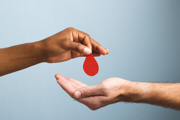 Hands of biracial man giving blood drop to caucasian man, on blue background - obrazy, fototapety, plakaty