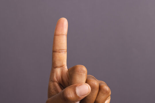 Hand of biracial man with outstretched forefinger, on grey background