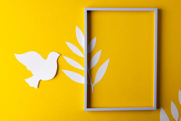 High angle view of white frame, white dove and leaves with copy space on yellow background