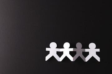 Close up of four paper cut out people figures holding hands with copy space on black background