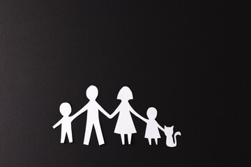 Fototapeta premium White paper cut out of family with two children and cat and copy space on black background