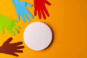 Paper cut out of multi coloured hands and white circle with copy space on orange background