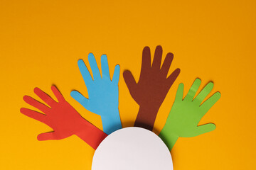 Paper cut out of multi coloured hands and white circle with copy space on orange background