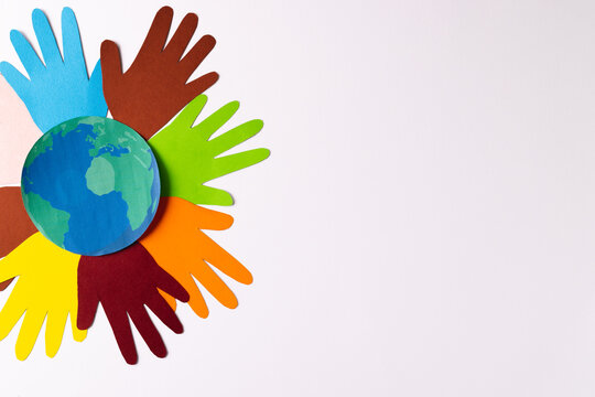 Paper cut out of multi coloured hands and globe with copy space on white background © vectorfusionart