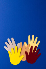 Close up of paper cut out of multi coloured hands with copy space on blue background