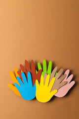 Close up of paper cut out of multi coloured hands with copy space on brown background