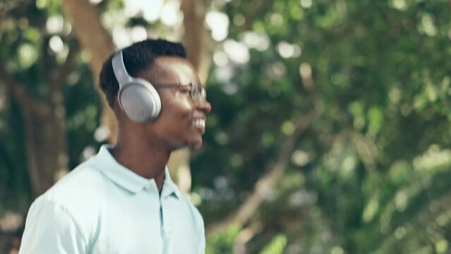 Happy, walking and a black man with music in nature for enjoyment, dancing and relaxation. Smile, dance and a young African guy with headphones for a podcast, audio and radio on a walk in a park