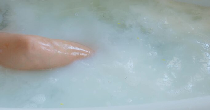 female raising her leg, knee while have milky bath. Relaxation and skin care. Spa procedure. slow motion. somebody pouring milk into bathtub, girl has fun at resort, hotel at weekend