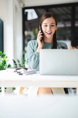 Vertical image of young confident businesswoman sitting at the office table working on laptop computer and smart phone mobile