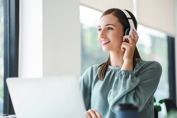 Relaxed young businesswoman in headphones enjoying music podcast using laptop app, smiling female millennial student or office worker wearing headset listening to new favorite audio tracks.