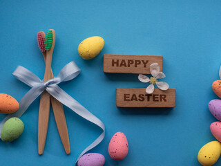 Happy Easter and dentist concept. Wooden toothbrushes with Easter decorations on blue background. Dentist Easter greating card. Top view, flat lay. Bamboo toothbrushes, colorful eggs, wooden words.