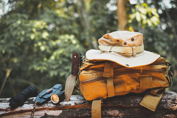 Equipment for survival bucket hat backpack hiking knife camping flashlight resting on wooden timber in the background is a forest - obrazy, fototapety, plakaty