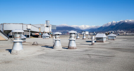Flat roof vents with hvac unit on building with modified bitumen roofing system with snowcapped mountains. Variety of metal ventilators such as: bathrooms and laundry exhaust and plumbing stack vent. - obrazy, fototapety, plakaty