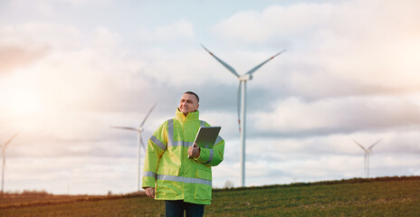 A male engineer man is standing in a wind turbine field with a beautiful sky background. Concept of sustainable future.