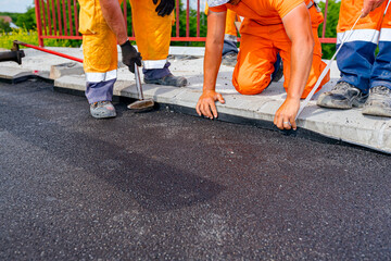 Workers apply black bitumen membrane strips for waterproofing roads and bridges to the curb of the sidewalk