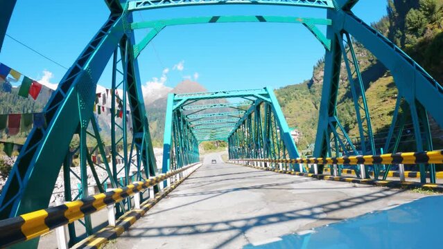 view of a car crossing metal bridge during sunny summer day in mountains at lahaul in himachal pradesh, india. road trip and transportation in travel concept.