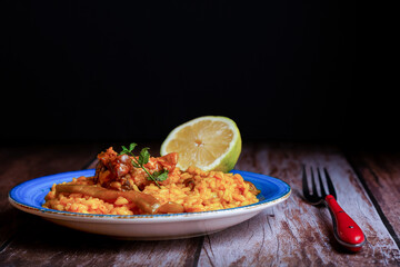 plate of paella with ribs and green beans, with bread, lemon and bottle of olive oil, isolated on black background