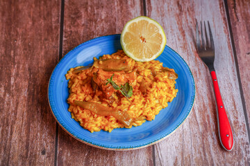 plate of paella with ribs and green beans , with lemon and fork on a wooden table