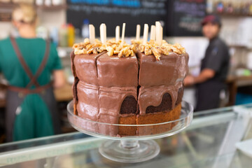 A vegan chocolate and banana layer cake sits in a glass cake stand on a cafe counter.