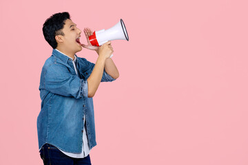Handsome Asian man in blue shirt shouting in megaphone announcing a sale. Hurry up isolated on pink background studio photo