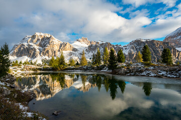 Fototapeta na wymiar Bergsee mit Felsmassiv, blauem Himmel, herbstlichen Bäumen und Eis und Schnee in den Dolomiten zum Sonnenaufgang.