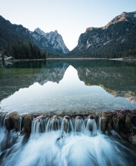 Wasserfall an einem See mit Spiegelung umrandet von hohen Bergen in Südtirol in den Dolomiten am...