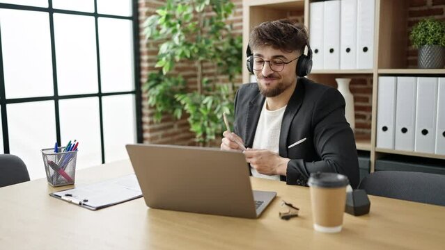 Young arab man business worker listening to music doing drummer gesture at office